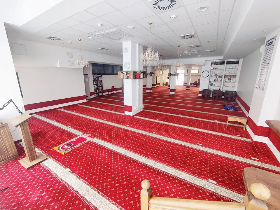 Der Gebetsraum der Moschee: roter Gebetsteppich mit hellen Bordüren, Kristallleuchter und Bücherregale